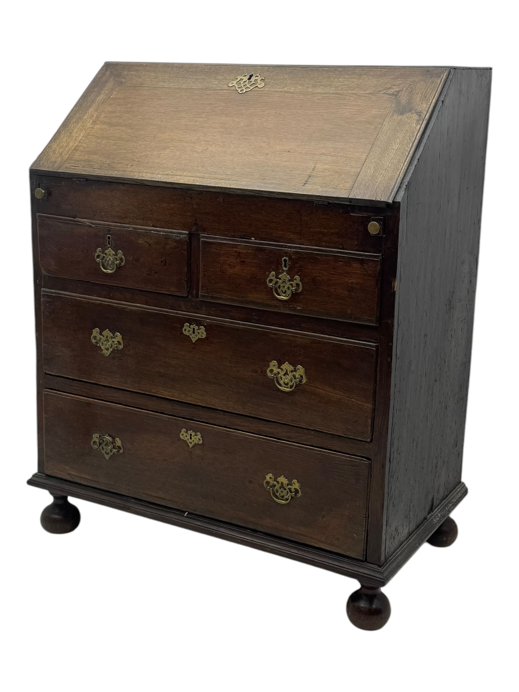 George III oak bureau, sloped fall-front enclosing a fitted interior with pigeonholes, small drawers, and a central compartment, over two short and two long drawers, brass escutcheons and drop handles, raised on bun feet