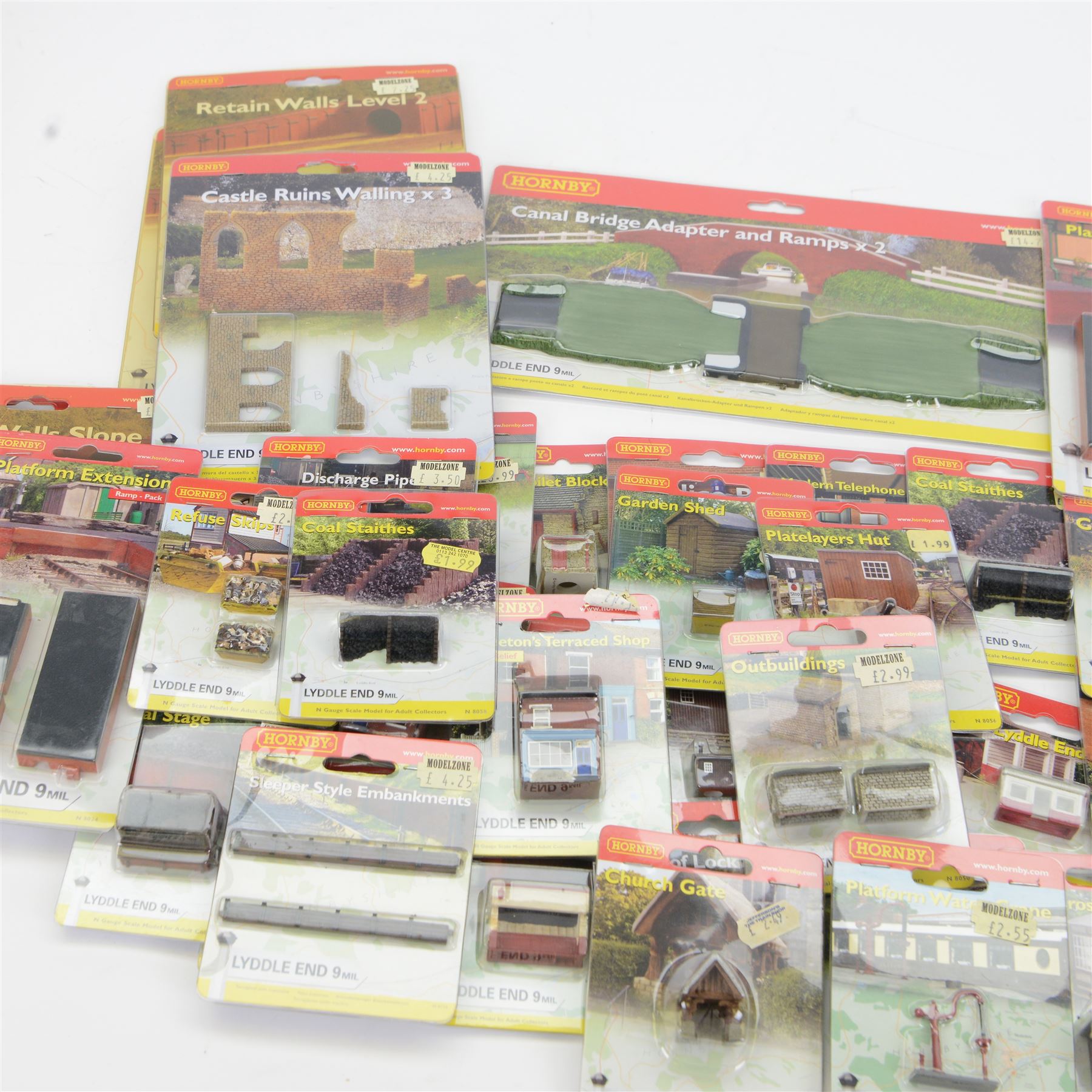 Forty-six Hornby N Gauge Lyddle End model railway trackside buildings and accessories, including N8574 Canal Bridge Adapter and Ramps, N8724 Castle Ruins Walling x 3, N8069 Tractors, N8018 Cotswold Stone Wall and N8096 Low Relief Terrace, all carded