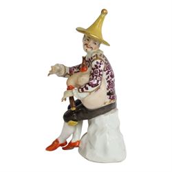 Mid 18th century Meissen figure, modelled as a harlequin playing bagpipes, circa 1745, possibly modelled by J.F.Eberlein after earlier models by J.J.Kändler, wearing a gilt edged tunic painted with flowers, black breeches with rosettes at the knees, red shoes and conical yellow hat, seated upon a rock, with traces of blue crossed swords mark beneath, H14cm