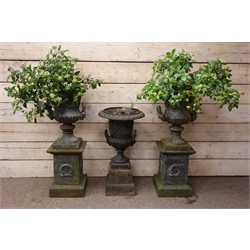  Pair of cast iron two-handled garden urns, lobed and scroll cast bodies on square bases and laurel wreath cast pedestals, H110cm, another similar urn with lion mask handles on plain tapering pedestal, H87cm (3)  