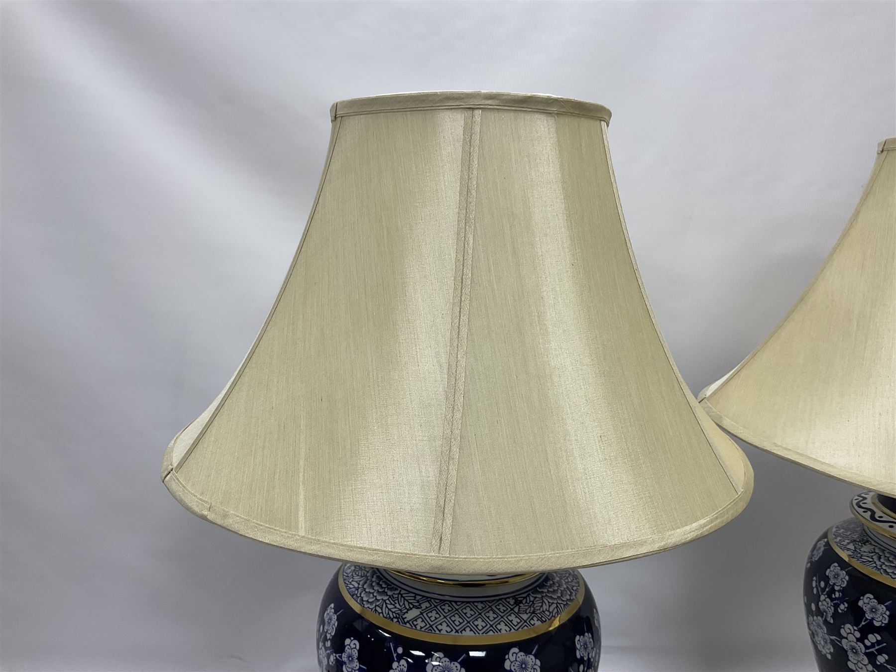 Pair of blue and white table lamps, each of baluster form, decorated with prunus blossom, within stylised borders, raised upon circular gilt base, excluding fittings H48cm