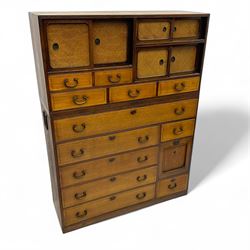 Late Meiji-period Japanese keyaki wood tansu chest, upper section with six sliding woven rattan doors over five drawers, lower section fitted with an asymmetrical arrangement of seven drawers and side cupboard with a hinged door enclosing three additional drawers, iron drop handles to sides