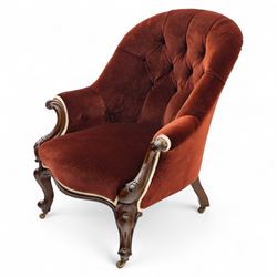 Victorian mahogany framed crimson velvet upholstered tub armchair, with buttoned back and scroll carved arms above a serpentine fronted seat rail, raised upon scroll carved cabriole front legs and plain curved back legs with brass castors 