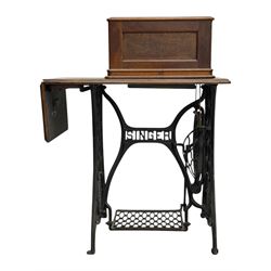 Singer - early 20th century cast iron treadle sewing machine, with hand crank wheel and oak work surface, the machine decorated with gilt foliate detail, complete with rectangular wooden cover and folding extension leaf
