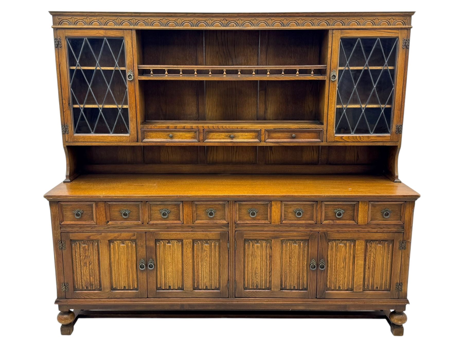 Large mid-20th-century oak dresser with two astragal glazed doors between gallery shelf and lower shelf, with three short drawers and lower section with four drawers and three double-panelled linen-fold hinged cupboard doors 