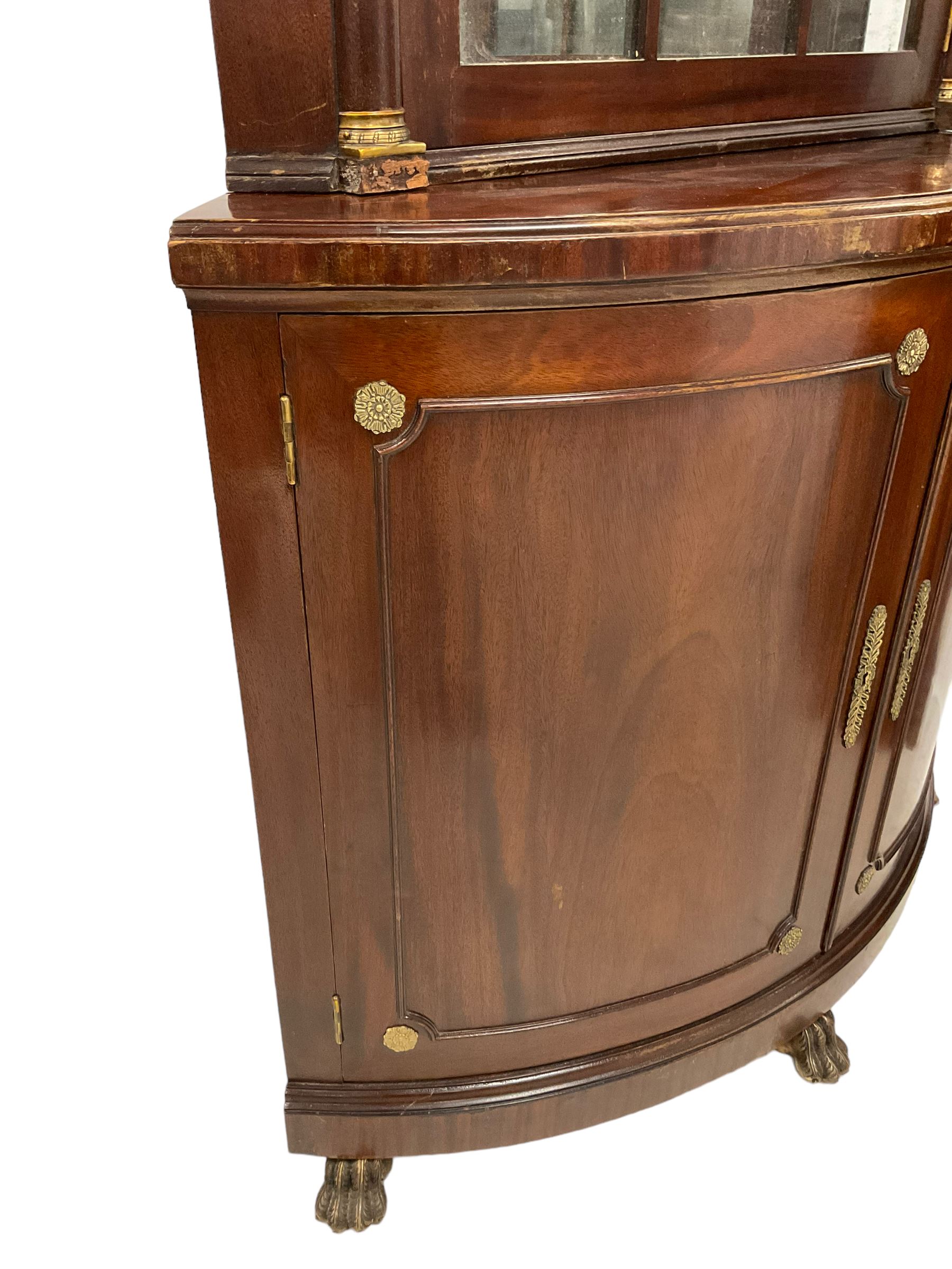 Pair of French Empire design corner cabinets, the straight-front upper section with canted corners and applied half-column pilasters, enclosed by mirror glazed door, the bow-front lower section enclosed by two doors with applied mouldings, mounted by cast metal floral rosettes, skirted base with cast gilt metal hairy paw brass feet