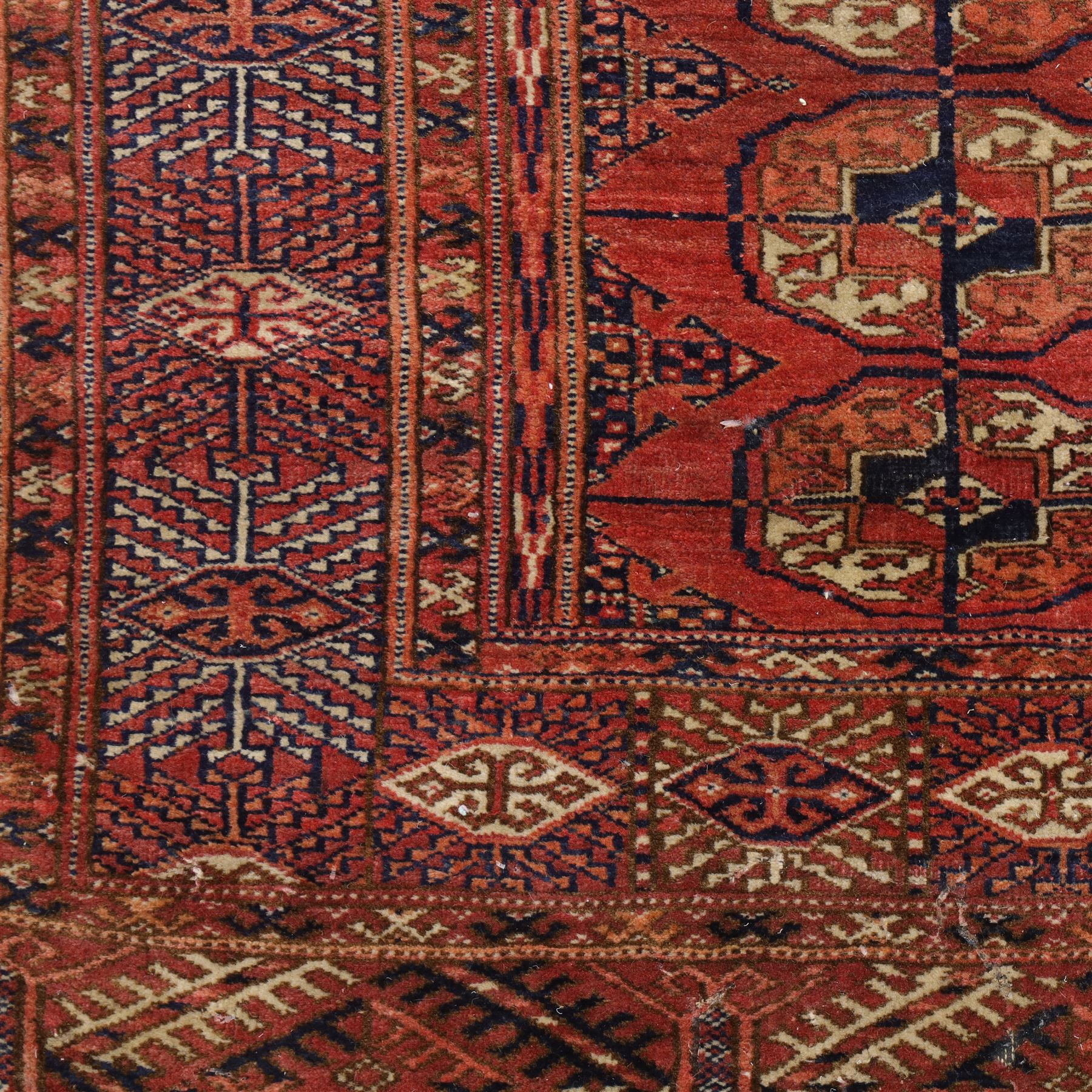 Central Asian Turkmen Tekke hand-knotted rug, madder red field decorated with rows of octagonal guls linked by secondary motifs within a dense geometric border, with fringe ends  