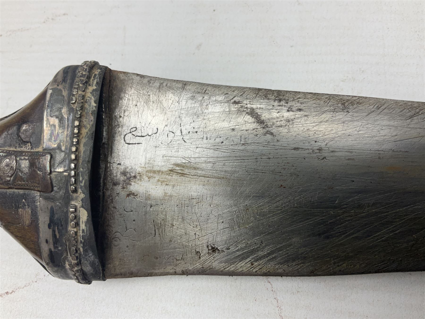 Late 19th/20th century Middle Eastern jambiya dagger the 36cm broad curved double edged steel blade with traces of script, horn and copper backed waisted white metal hilt with three roundel buttons; in ornate white metal and leather mounted brass and steel scabbard L60.5cm overall