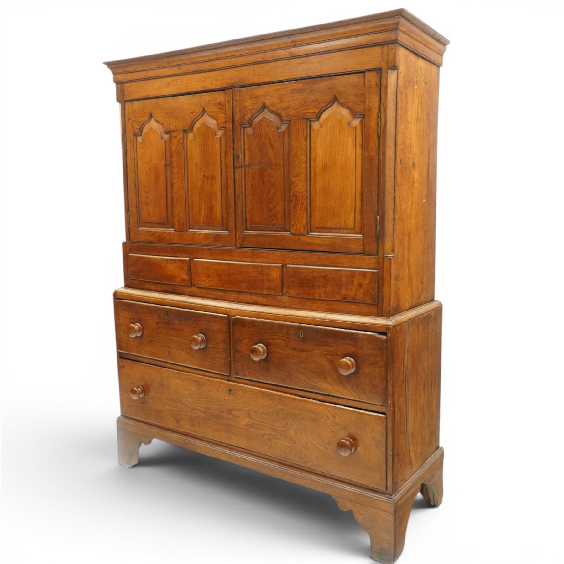 18th century oak larder cupboard, projecting moulded cornice over two panelled doors with shaped arched fielded panels, three short dummy drawers above base fitted with two short and one long drawer, turned handles, on bracket feet