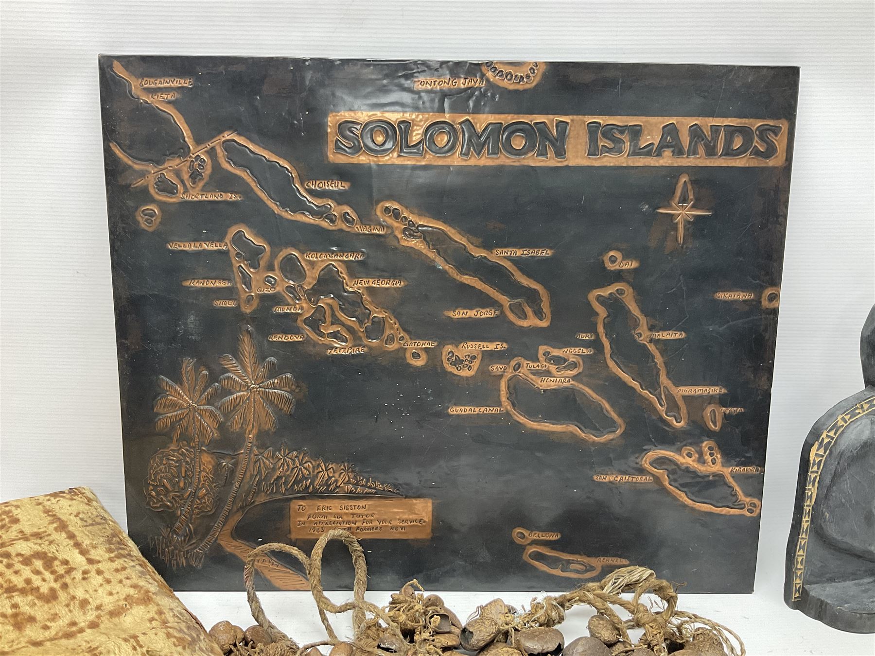 Collection of traditional necklaces from the Solomon Islands, including shell and boar tusk examples, together with a carved canoe prow, with mother of pearl eyes, painted cow hide and a copper plaque, depicting the Solomon Islands, with presentation engraving
