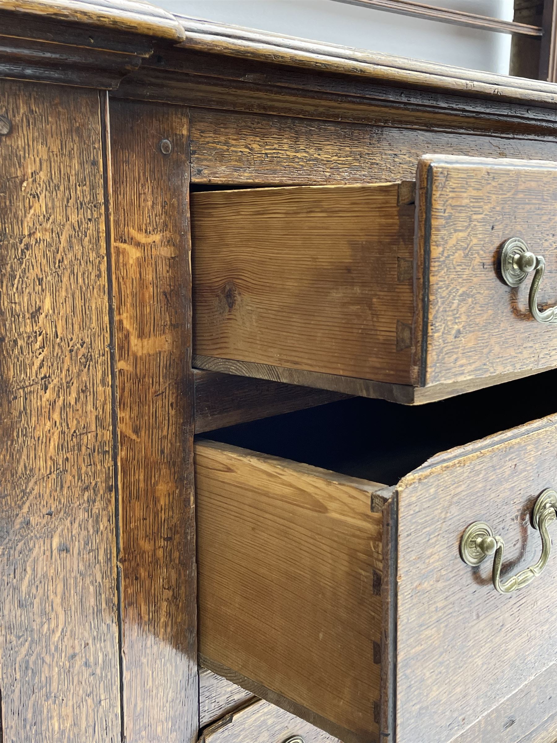 George III oak dresser, projecting dentil cornice over three heights plate rack enclosed by fluted uprights, the dresser fitted with five drawers and two panelled cupboards, canted corners with fluted quarter columns, on bracket feet