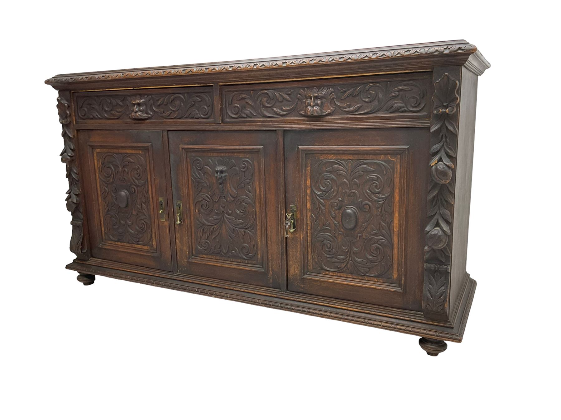 Victorian heavily carved oak sideboard, the moulded top carved with foliate decoration to the edge, fitted with two drawers and three cupboards, the drawer fronts carved with green man mask handles and scrolling foliage, the panelled doors carved with interlacing foliage, on turned compressed bun feet