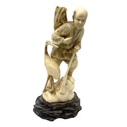  Japanese Tokyo School ivory figure, 19th century, carved as a man stood upon a rock carrying firewood and a gun, next to a crane, upon a carved wooden base, H25cm