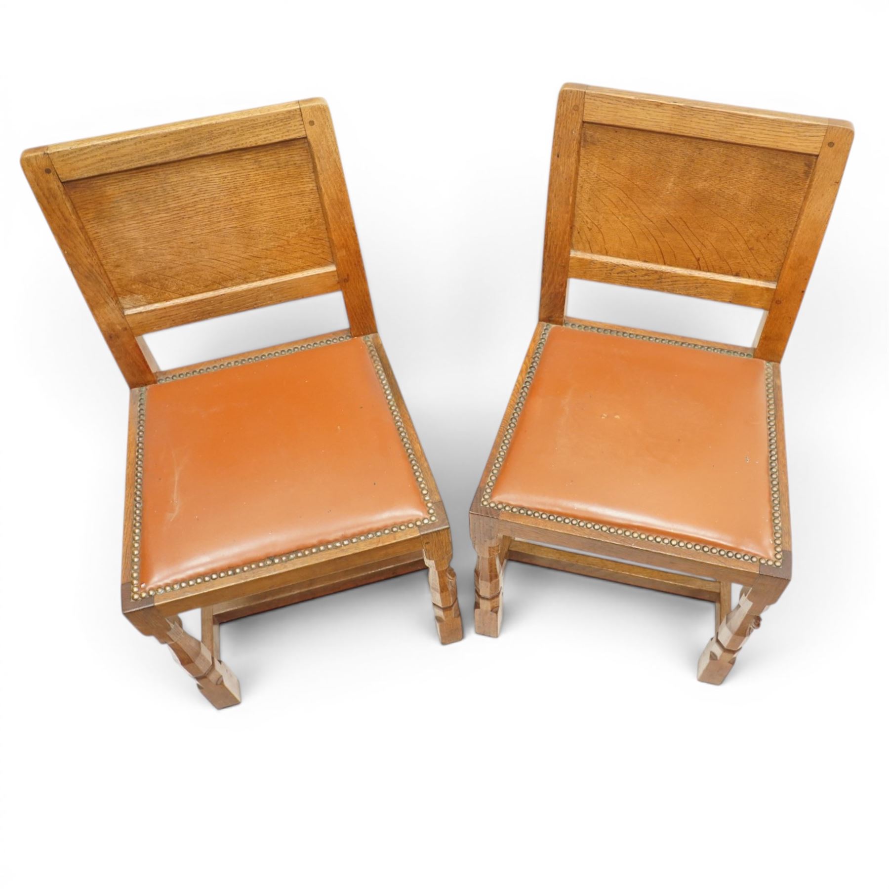 Mouseman - pair of 1940's adzed and panelled oak chairs, the rectangular adzed back-panel over seats upholstered in orange-tan leather with studwork, raised on turned octagonal supports united by box stretcher, with carved mouse signature, by the workshop of Robert Thompson of Kilburn
Provenance: purchased directly from the Kilburn workshop in the late 1940s