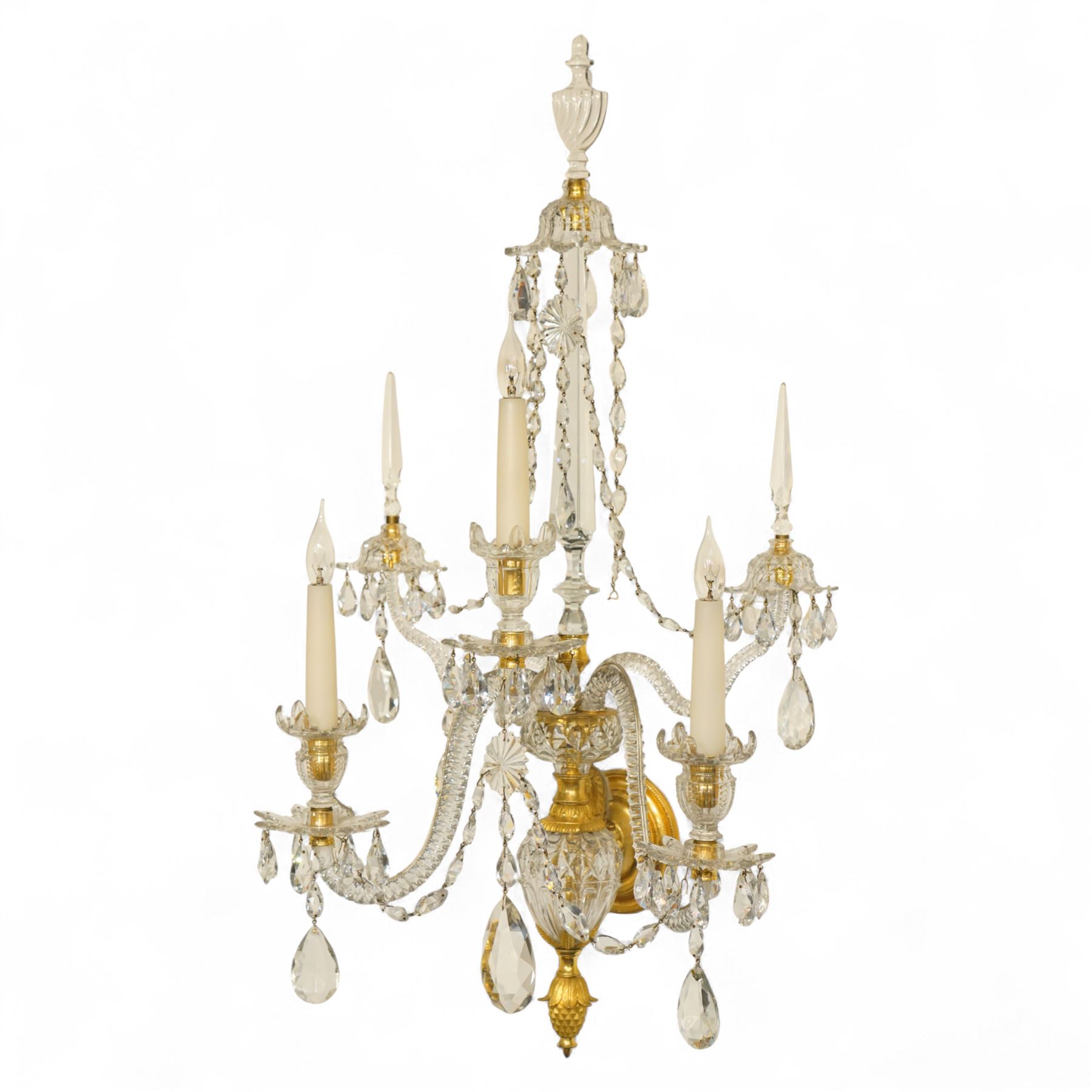Pair of George III ormolu and cut-glass wall-lights, each with a tall central urn-shaped finial above a series of faceted glass spires and scrolled branches, the ormolu-mounted nozzles and drip pans hung with festoons of cut-glass drops and pear-shaped pendants, the lower section centred by a pineapple finial, wired for electricity