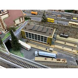 Table top 'N' gauge continental scenic layout as a split level town with various loops of track, station with numerous platforms, engine shed, assorted buildings, roads with motor vehicles and figures, tunnels, trees, river with bridge, tram depot etc 122 x 52cm