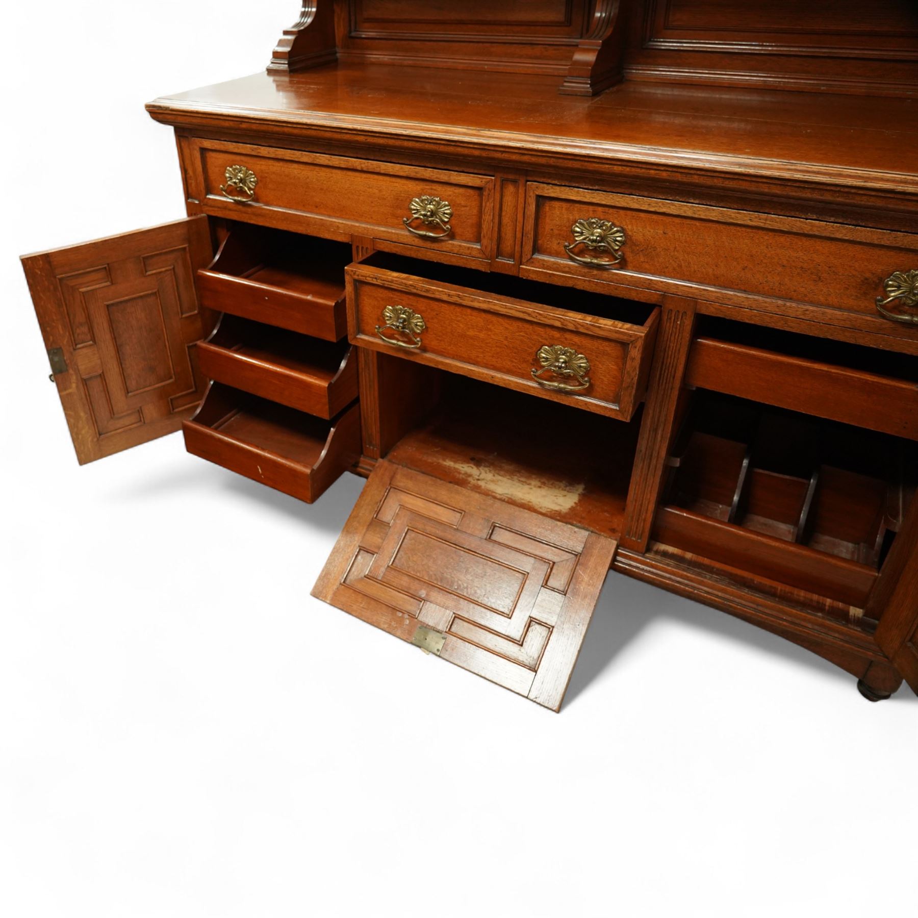 Early 20th century golden oak dresser sideboard, superstructure with three stained and leaded glass doors flanked by carved uprights above an open display shelf, the base with three drawers and geometric panelled cupboard doors, enclosing drawers with cutlery and bottle compartments, raised on short feet