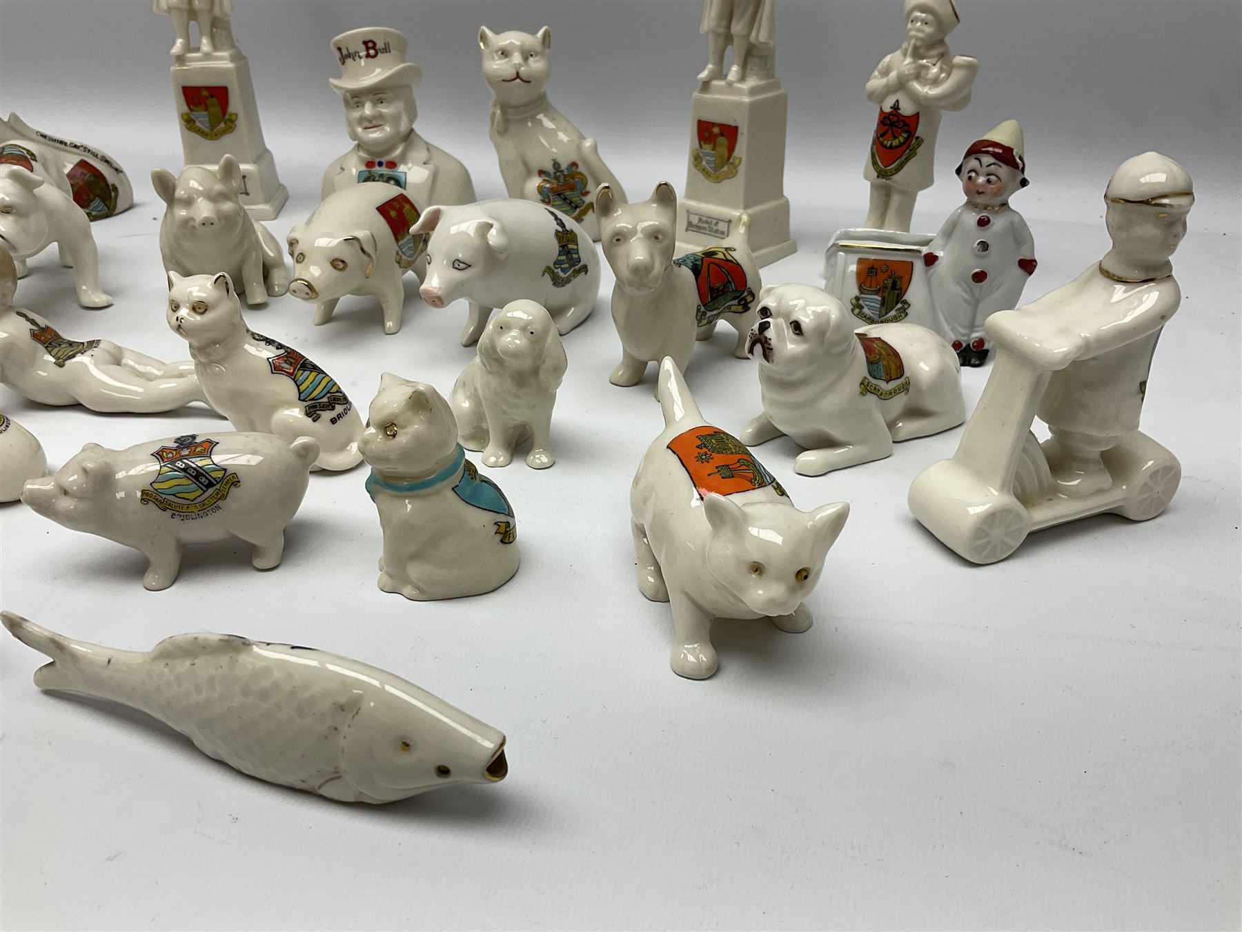 Collection of figural crested ware, to include Carlton Chins John Bull Alnwick, Clifton China Cheshire Cat,  Arcadia pig, Crafton crawling baby and another seated baby, quantity of cat, dog and pig figures, two Willow Art Model of Bunyans Statue, Toby jug, Victoria China, Arcadan bulldog, fish etc