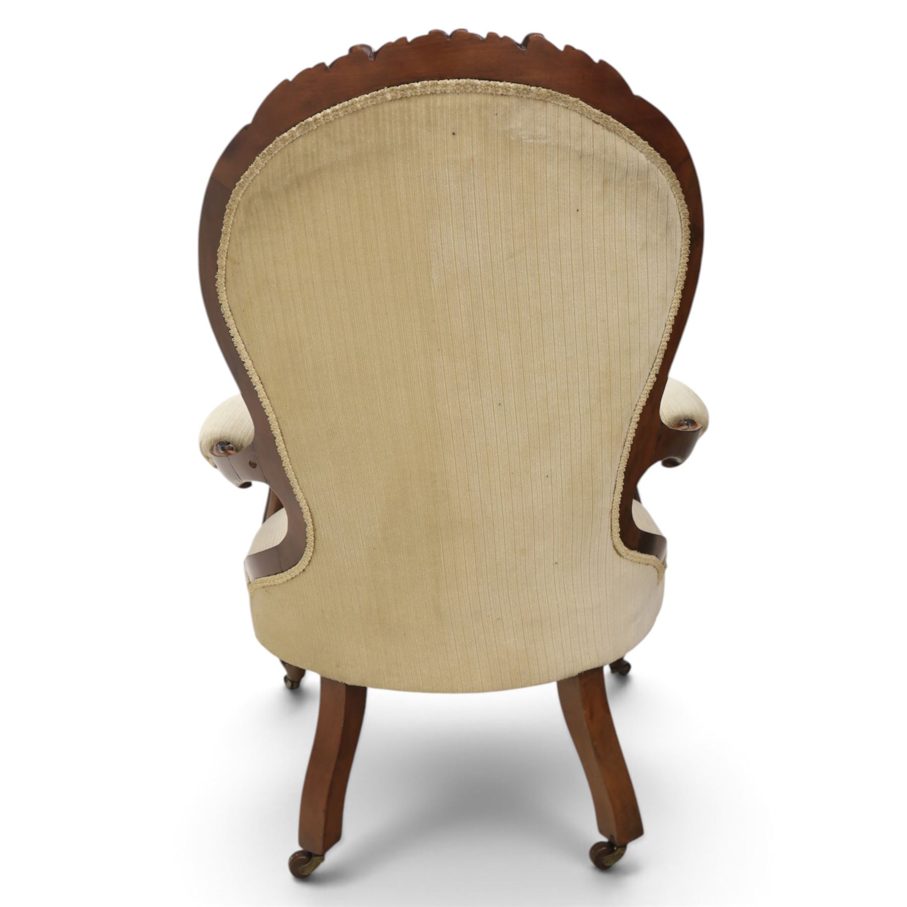 Late Victorian walnut open armchair, the carved shaped cresting rail centred by scrolls and foliage above a padded serpentine back and overstuffed seat upholstered in cream striped fabric, with padded scroll arms on open carved supports, raised on cabriole supports with carved knees and ceramic castors