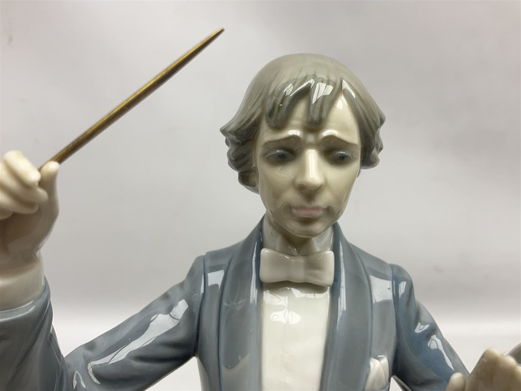 Two Lladro figures, comprising Conductor no 5196 and Prayerful Moment no 5500 together with a Lladro plaque and two Lladro candle holders, Dolphins at Play no 17666 and Sailing the Seas no 17665, all with original boxes, largest example H33cm 