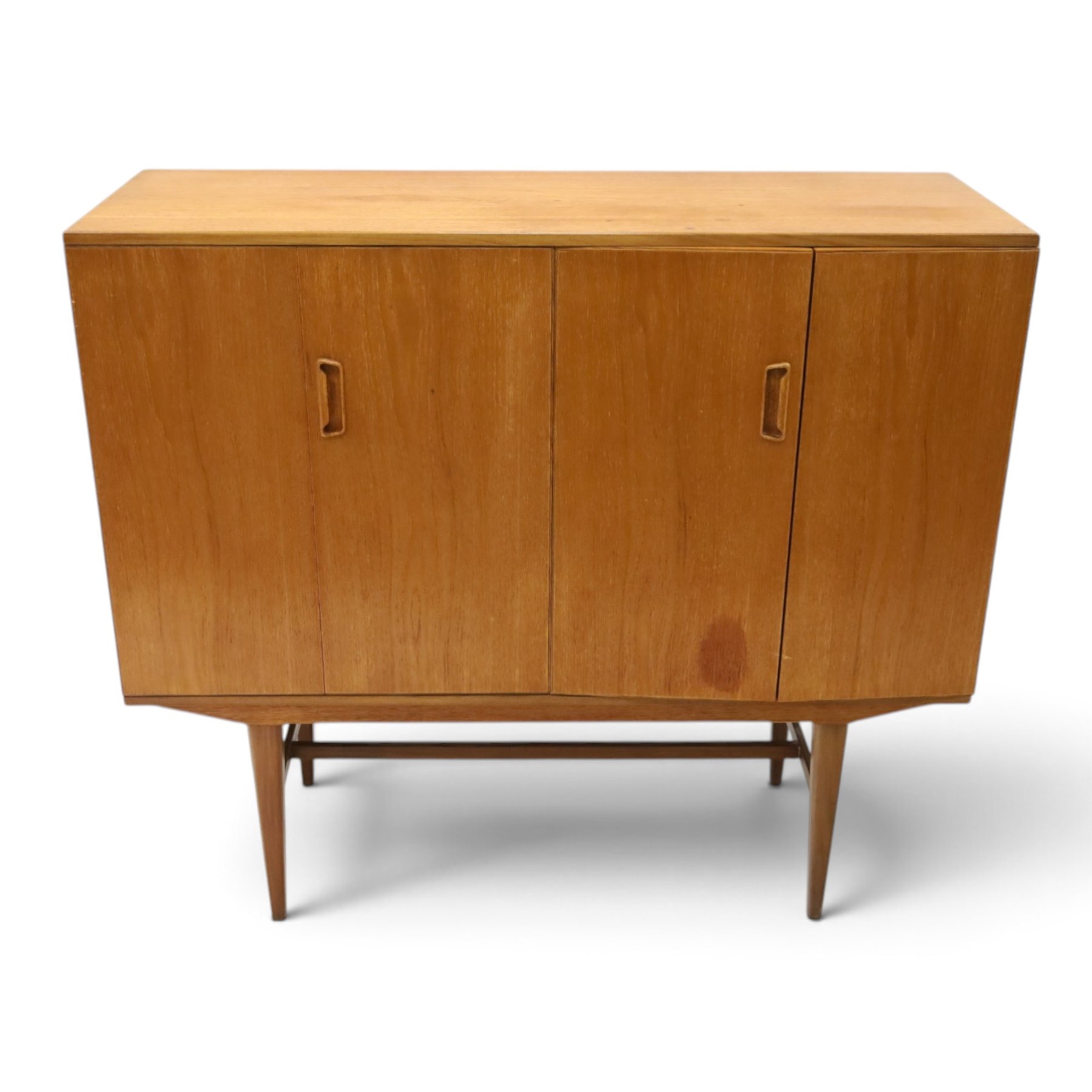 Alfred Cox - mid-20th century teak cabinet, rectangular top over two bifold doors with inset handles, opening to reveal three central graduating drawers surrounded by assorted shelves, raised on tapering supports united by H-stretcher, stamped to inside of drawer