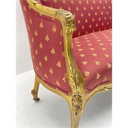 Victorian carved giltwood settee, the shaped cresting rail decorated with shell cartouche and flower head motifs, down swept arms with acanthus leaf and scrolled terminals, upholstered in red ground fabric decorated with repeating gilt motif pattern, cabriole supports with brass castors 