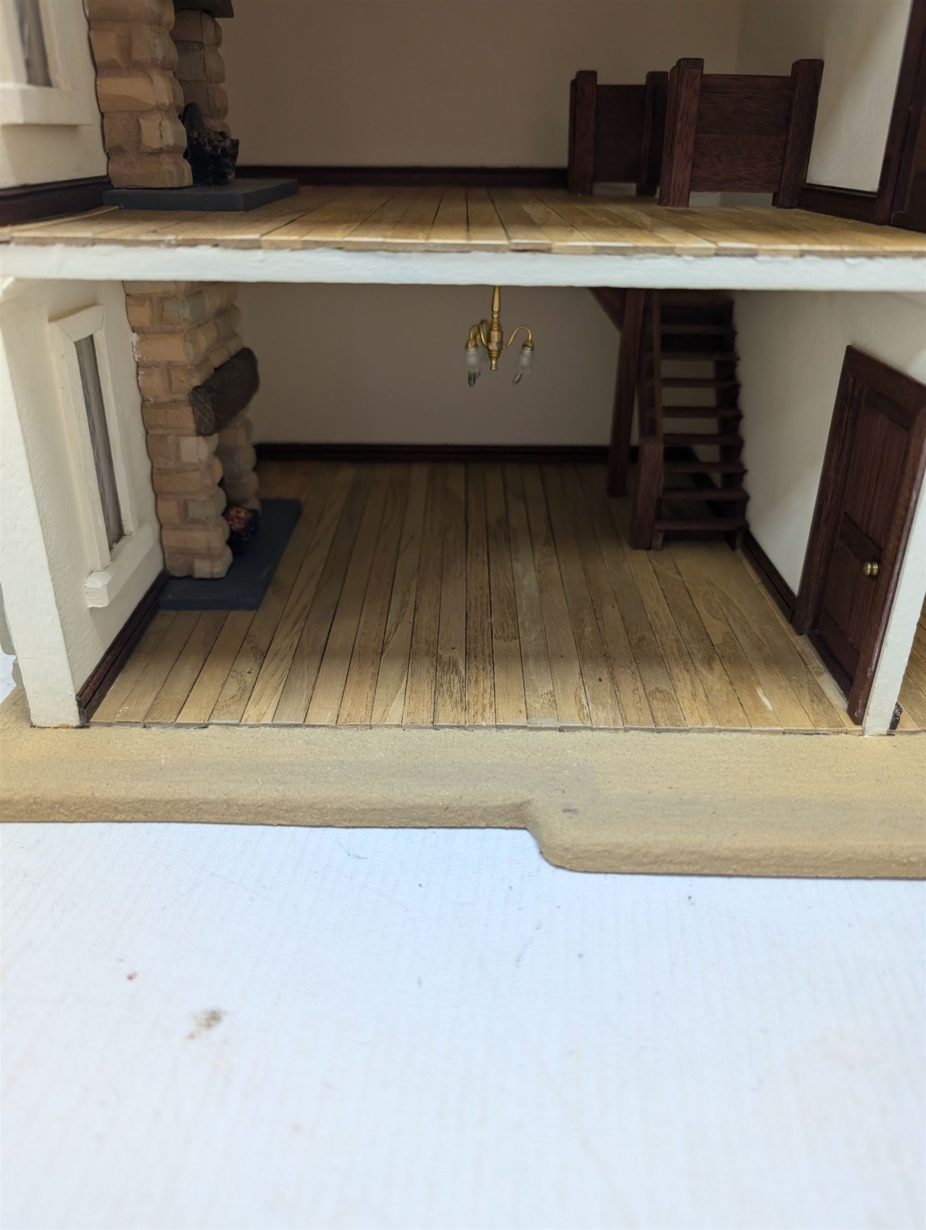 1:24 scale stone effect three-storey cottage dolls house, with green arched door and lattice effect windows, decorated to the interior with wooden floors, wired lighting and fire places, H45cm, W57cm, D26cm