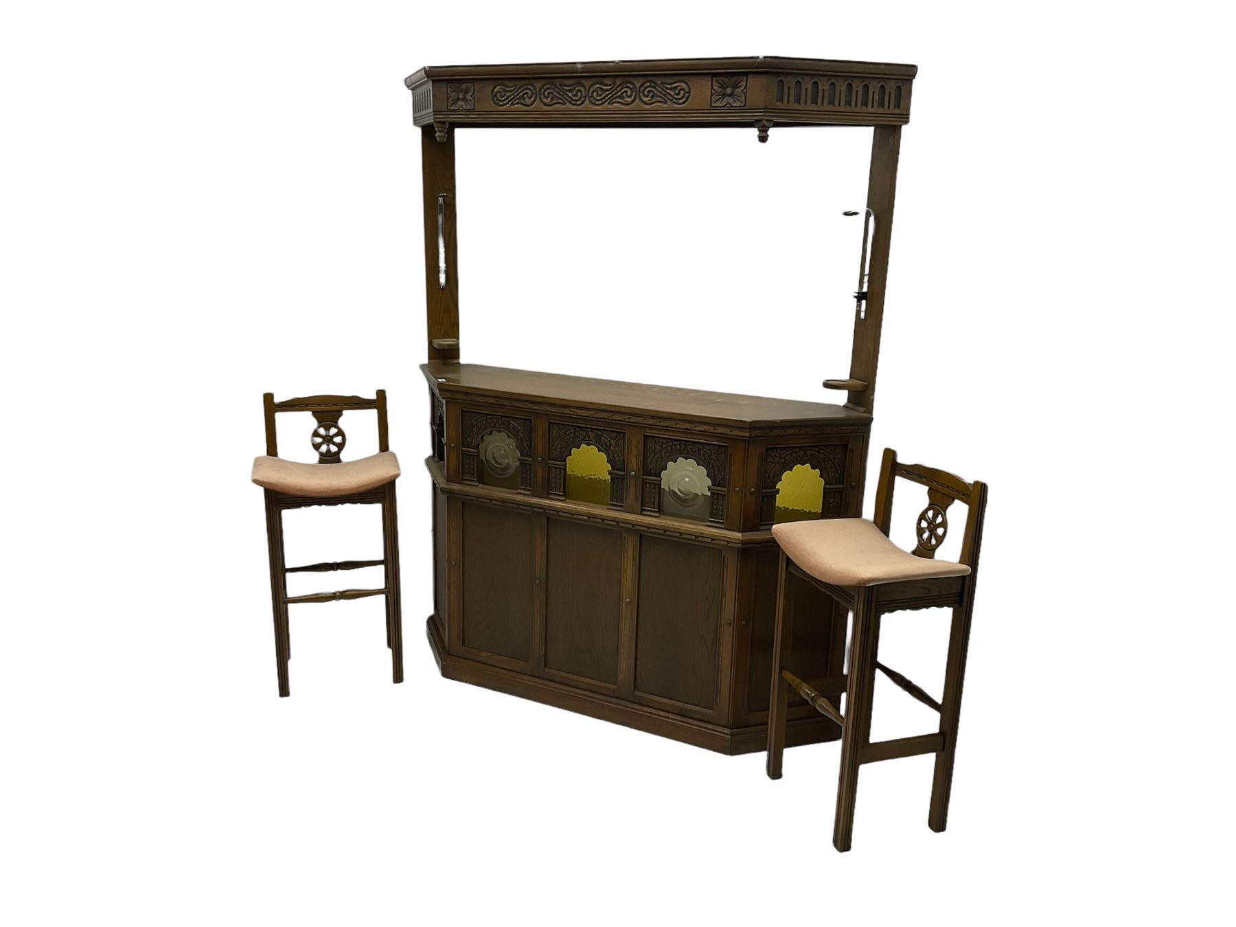 Old Charm - oak corner bar, the canopy frieze carved with scrolls, front decorated with arched apertures glazed with bullseye and mottled glass panes, skirted base, together with two bar stools