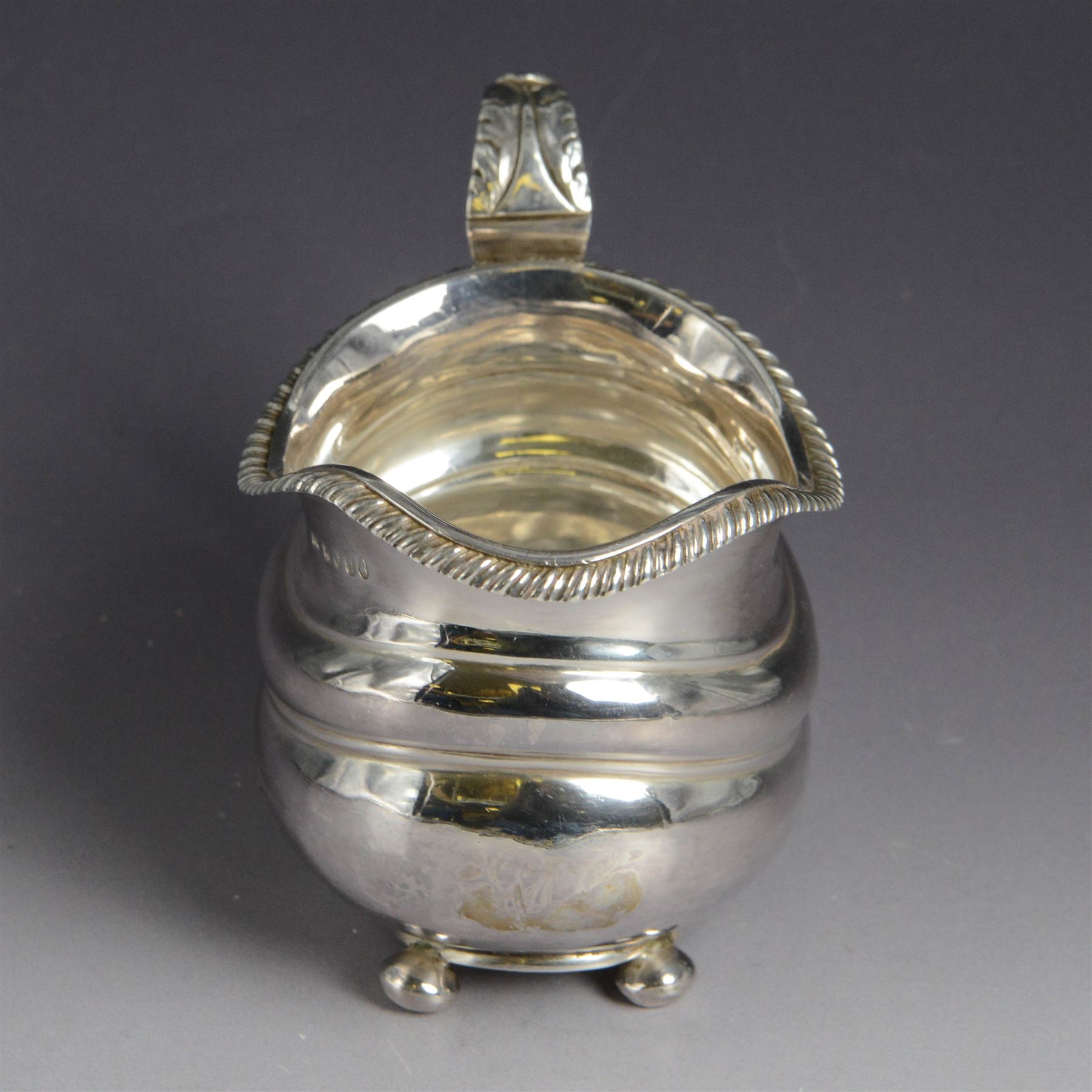 George III silver milk jug, of oval form with oblique gadrooned rim and acanthus leaf capped handle, upon four bun feet, hallmarked London 1819, maker's mark worn and indistinct, H10cm