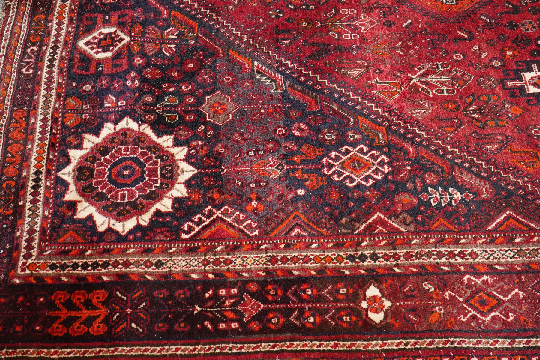 Large Persian Shiraz crimson ground carpet, the busy field decorated with a geometric pole medallion surrounded by stylised plant motifs with contrasting indigo spandrels and geometric-woven guard bands