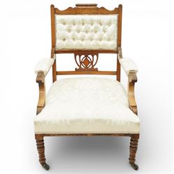 Edwardian mahogany open armchair, the upholstered rectangular back buttoned in ivory patterned fabric within a shaped top rail with inlaid foliate detail, open splat carved with a pierced anthemion motif centred by an inlaid roundel, swept open arms with upholstered pads, over a sprung upholstered seat, on turned front supports with brass castors