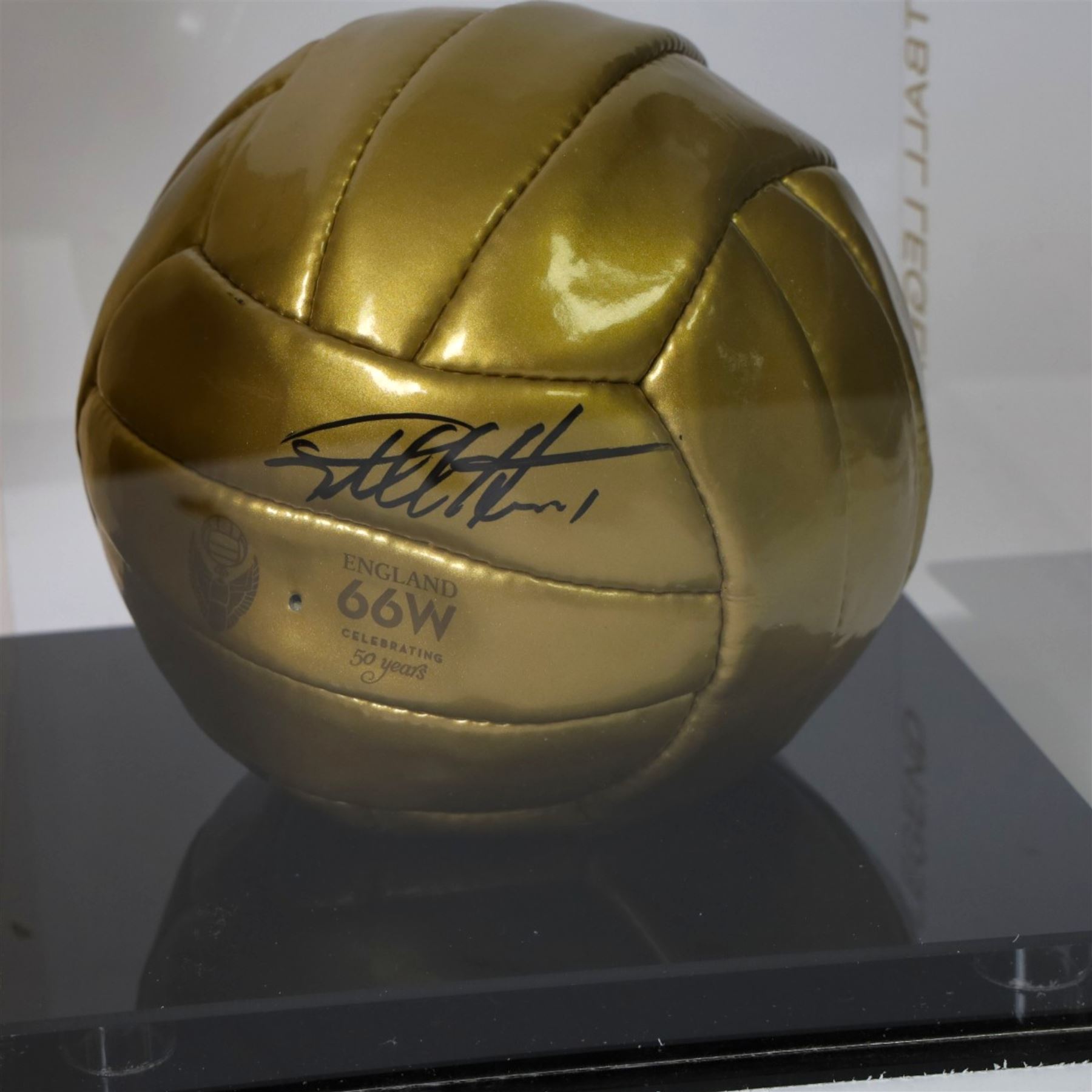 Limited edition football signed by Geoff Hurst to commemorate 50 years since England won the Football World Cup in 1966, a gold coloured football signed in black marker pen to one side, the ball stamped England 66W Celebrating 50 Years, contained within a Perspex display case, with certificate of authenticity from Northern Promotions