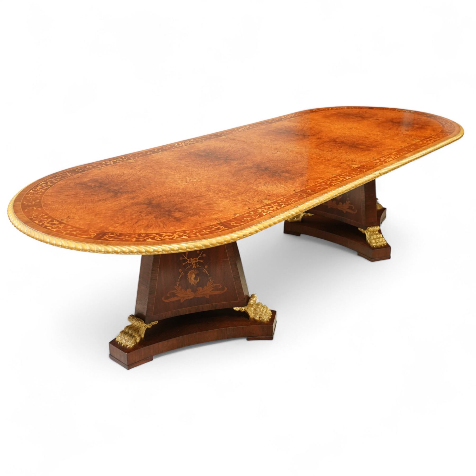 Arthur Brett & Sons - late 20th century twin pedestal dining table in the Second Empire style, the oval Amboyna burl veneered top, bordered with tulipwood crossbanding and delicate floral marquetry inlay, and rosewood crossbanded outer border within gilt gadrooned edge, over two mahogany triform pedestal bases with rosewood crossbanding and decorated with neoclassical marquetry of tied ribbons, leafy sprays, and scrolling acanthus decoration, raised on carved and gilded lion paw terminals on plinth bases, underside with maker's label