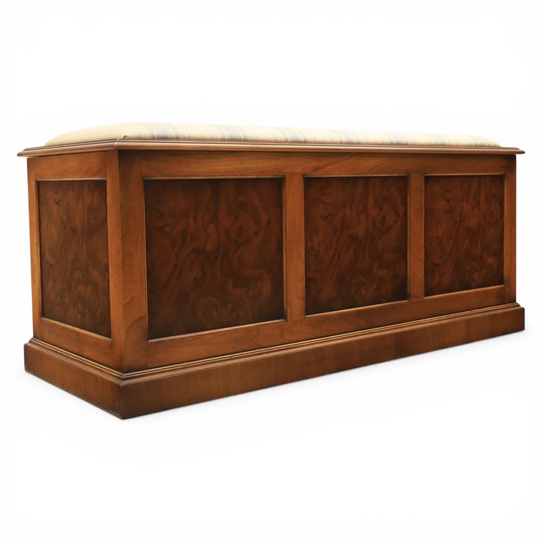 Traditional design figured elm blanket chest, with padded striped upholstered seat, over a hinged top with panelled sections below raised on a plinth base