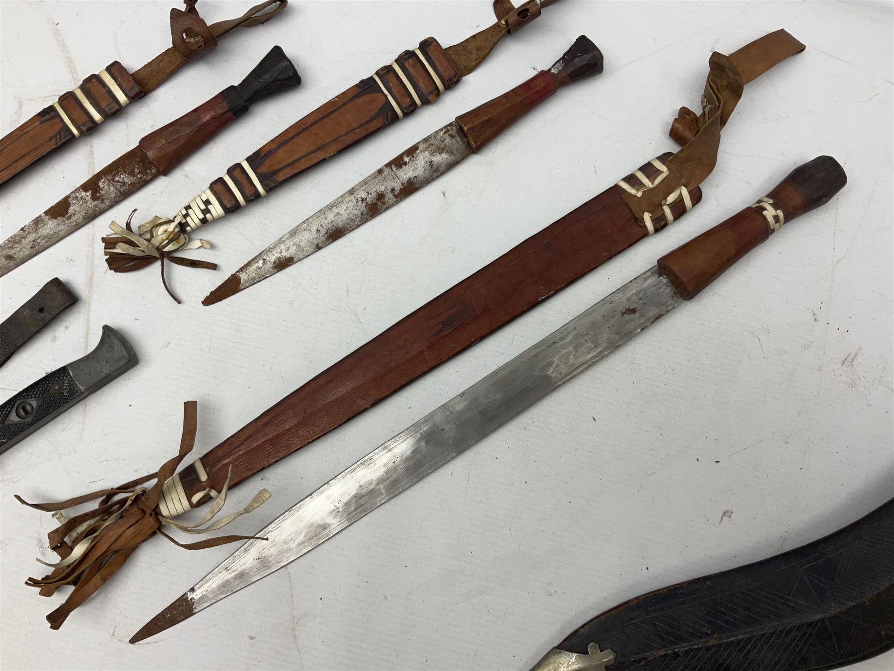 Indian kukri with 29cm curving steel blade and nickel mounted horn grip; in leather covered scabbard with one skinning knife L42cm overall; Hitler Youth knife with scabbard in relic condition; and three African graduated knives each with crudely carved wooden grips and painted leather covered scabbards (5)