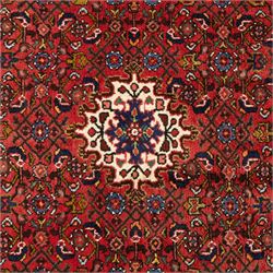 Hamadan hand-knotted rug, red field with small central floral medallion and dense repeating geometric motifs in dark blue, cream and green tones, within multiple patterned borders