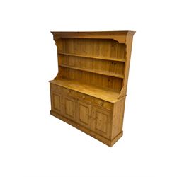 Rustic pine dresser, projecting cornice over two plate racks with shaped end supports, fitted with four drawers over four panelled cupboard doors, on plinth base