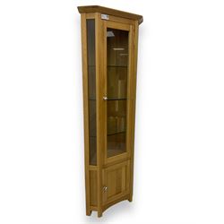 Contemporary light oak corner display cabinet, projecting cornice over single glazed door enclosing three glass shelves, the base fitted with panelled cupboard enclosing single oak shelf, on stile supports