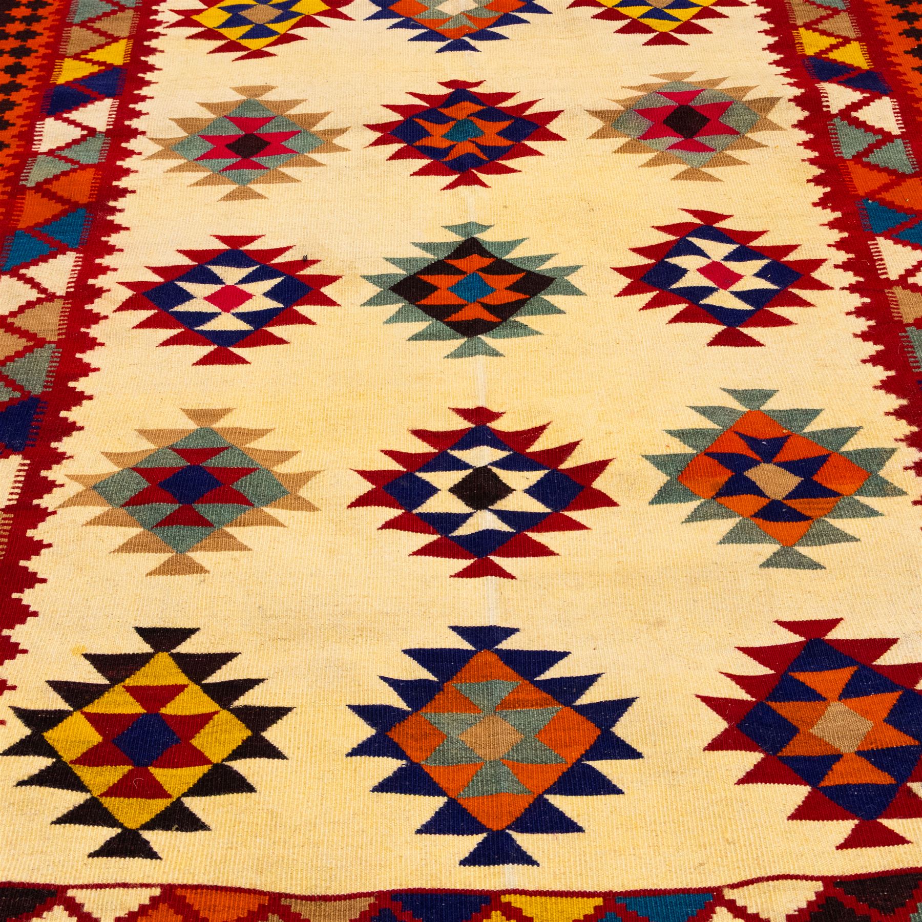 South West Persian Qashqai flatweave kilim, ivory field decorated with rows of multicoloured stepped diamond medallions composed of angular geometric motifs, enclosed by bold polychrome borders of triangular devices and stylized geometric, ornamentation, with fringe ends 
