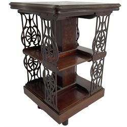 Edwardian mahogany revolving bookcase, the shaped moulded top inlaid with cusped panel and trailing bellflowers within a satinwood frame, foliate pierced upright splats and central square column supporting two tiers, on cruciform base with brass and ceramic castors 