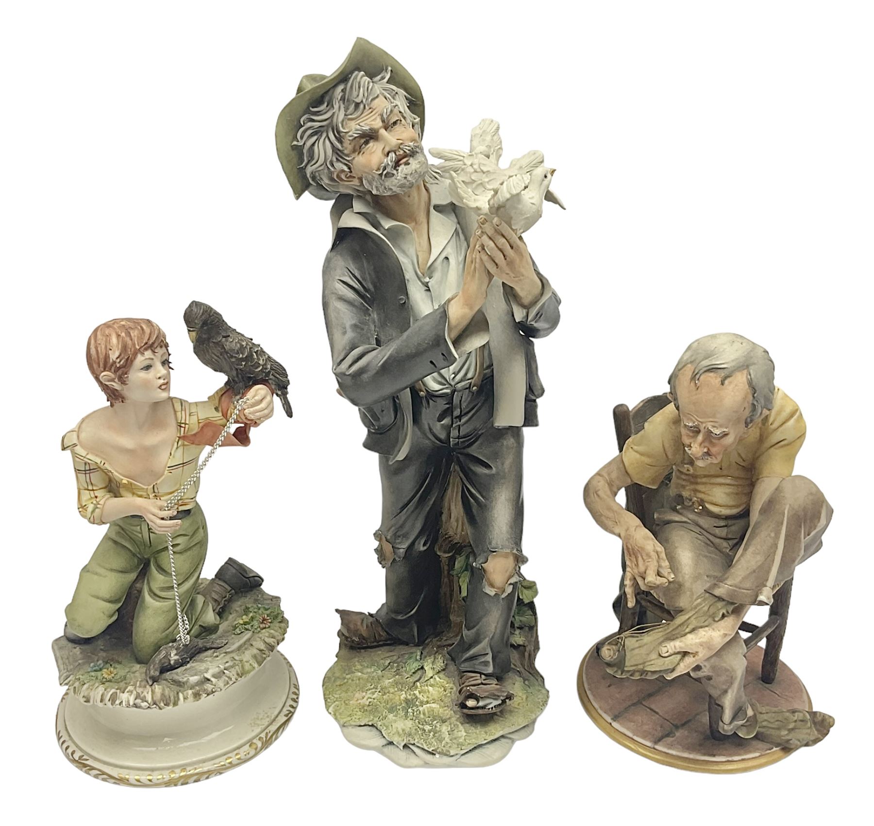 Three Capodimonte figures, to include The Kind Heart Man, modelled by Cortese as a tramp with two doves, The Young Falconer by Maria Angela and another modelled as a tramp darning his socks, all with printed marks, tallest H39cm