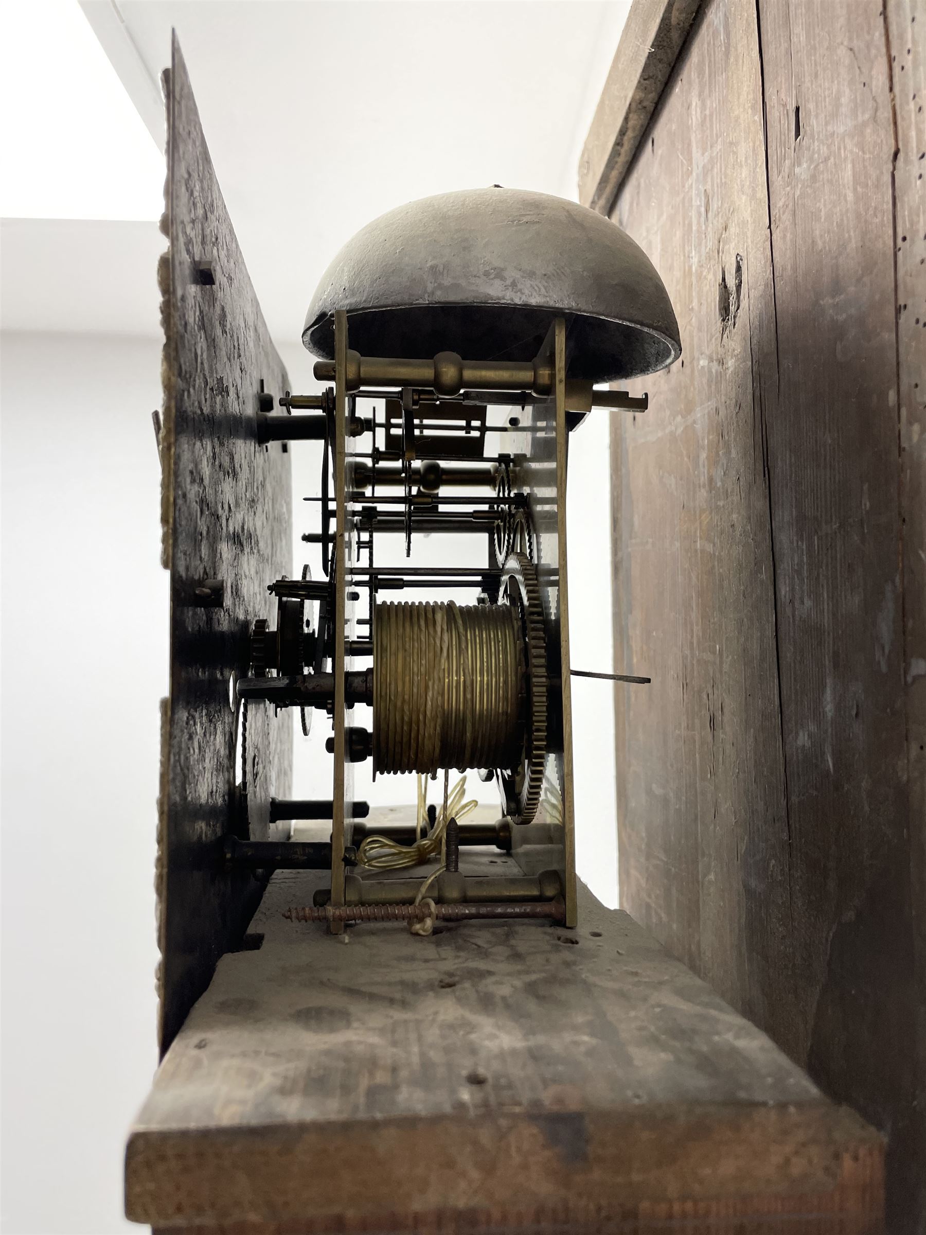 19th century carved oak longcase clock, projecting cornice over guilloche carved frieze, square brass dial with silvered Roman chapter ring and calendar aperture, decorated with ornate mask cast spandrels, the trunk door and base carved with potted plant, twin train driven eight day movement striking on bell