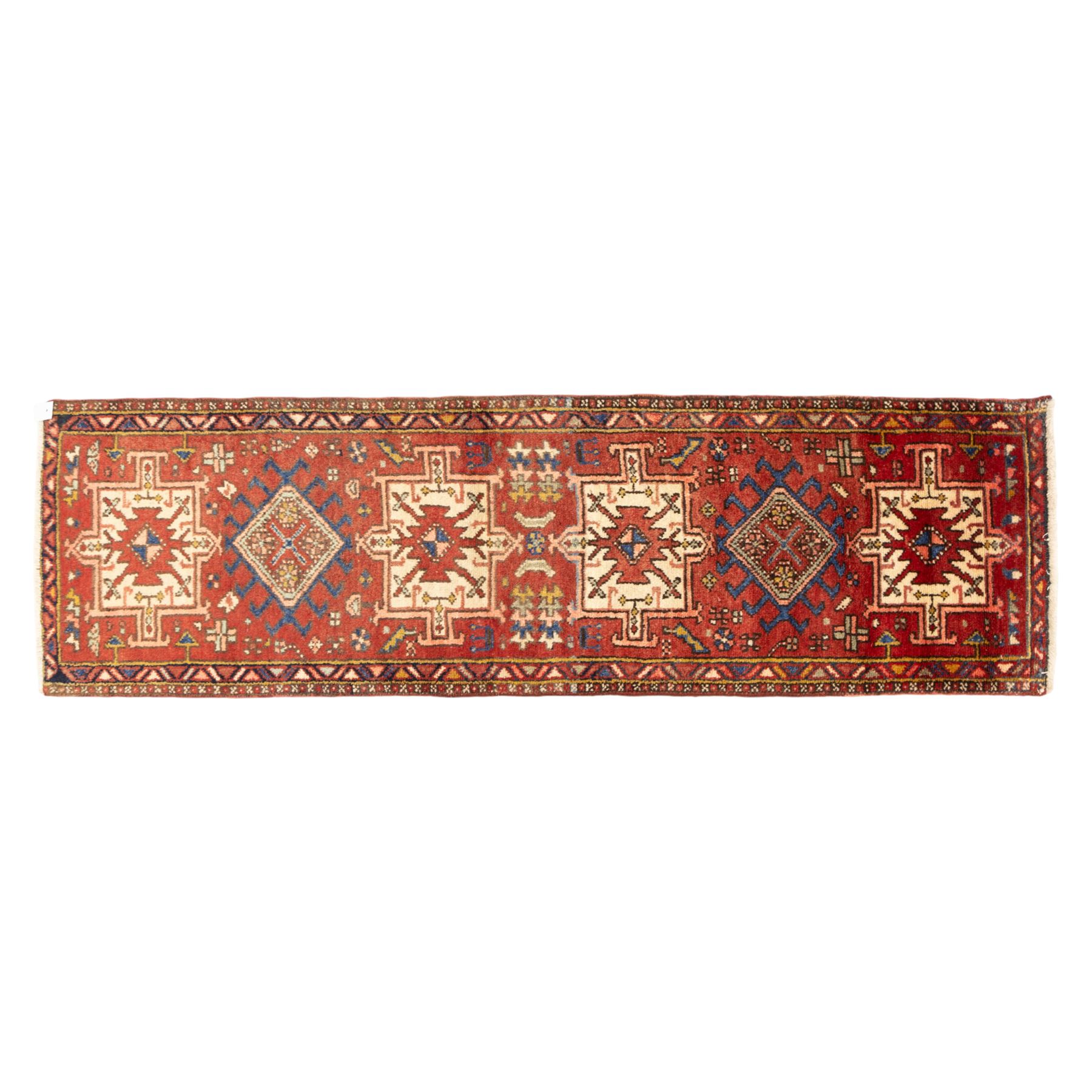 North west Persian Heriz runner, madder red field with a single column of alternating hooked and stepped lozenge medallions in ivory, blue, and terracotta, scattered with small cruciform and geometric motifs within a brick red border, angular motifs between narrow guard stripes 
