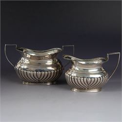 Victorian silver bachelors teapot, of part fluted oval form with ebonised wooden handle and finial, hallmarked Thomas Bradbury & Sons, London 1896, together with a Edwardian silver milk jug and open sucrier, of similar form with oblique gadrooned rims, hallmarked George Unite, Birmingham 1902 & 1906