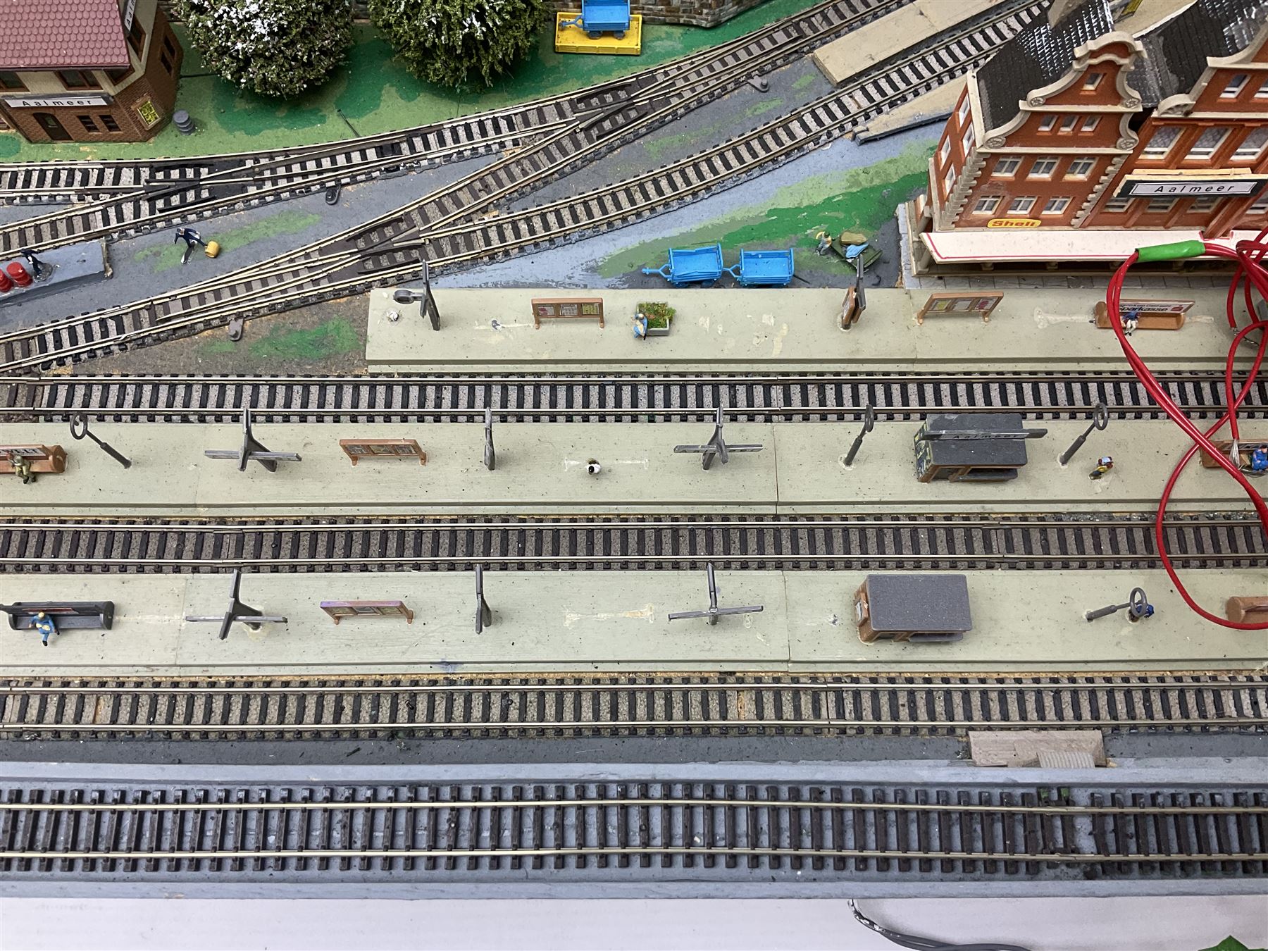 Table top 'N' gauge continental scenic layout as a split level town with various loops of track, station with numerous platforms, engine shed, assorted buildings, roads with motor vehicles and figures, tunnels, trees, river with bridge, tram depot etc 122 x 52cm