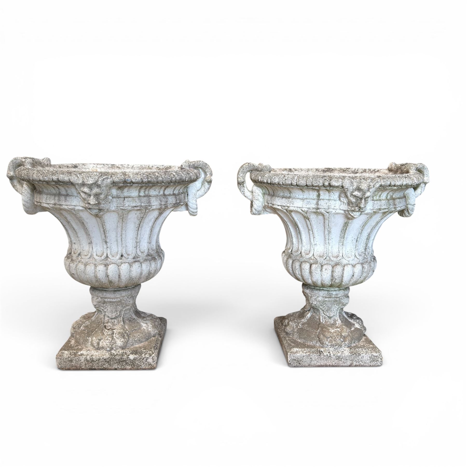 Pair of Neoclassical design cast stone garden urns, each of campana form with fluted body and gadrooned underbelly, decorated with faun/satyr opposing masks and ropetwist handles, with floral and mask design to the socles, raised on square bases, finished in weathered white patina