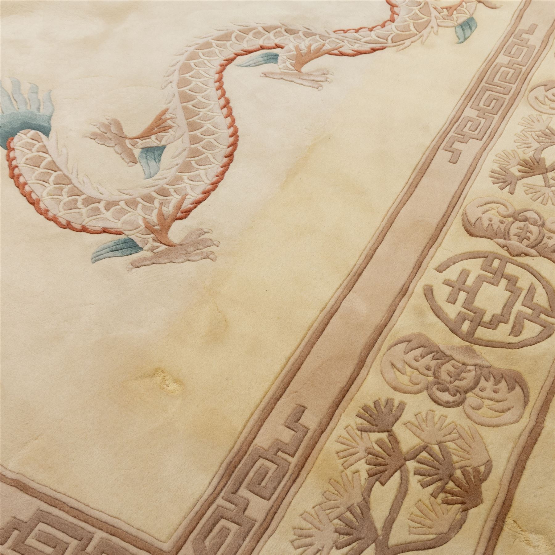 Late 20th century Chinese wool carpet, cream field with five stylized dragons arranged in a circular formation around a central flaming pearl motif, dragons depicted with elongated bodies and clawed feet amongst stylized cloud forms, enclosed within a narrow inner border and a wider outer border decorated with traditional Chinese motifs and symbols