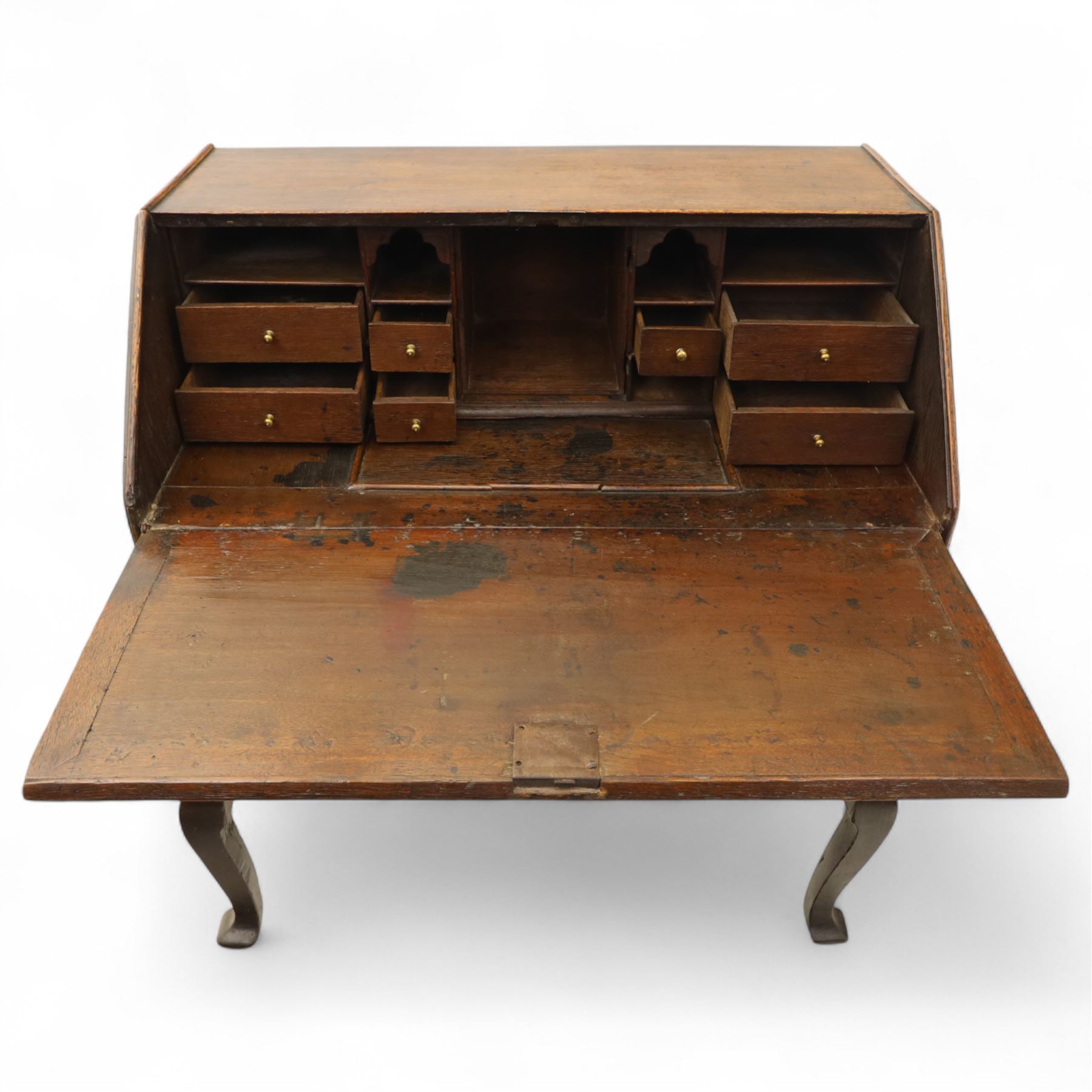 Early 18th century George I oak bureau on original stand, the fall front enclosing an arrangement of correspondence drawers and pigeonholes over central well, fitted with single long drawer below, the shaped apron over cabriole supports with pad feet