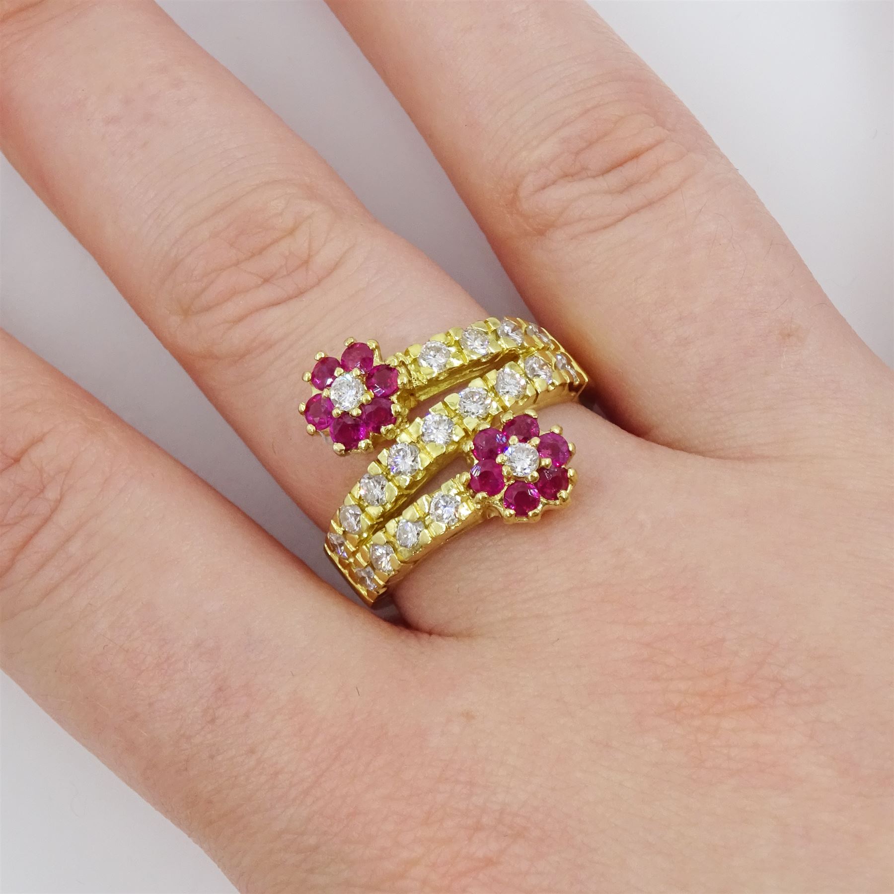 18ct gold ruby and diamond flower head crossover ring, two flowers each set with a single round brilliant cut diamond and six rubies, to diamond set stems and spaced by a row of nine diamonds, stamped 750, total diamond weight approx 0.55 carat