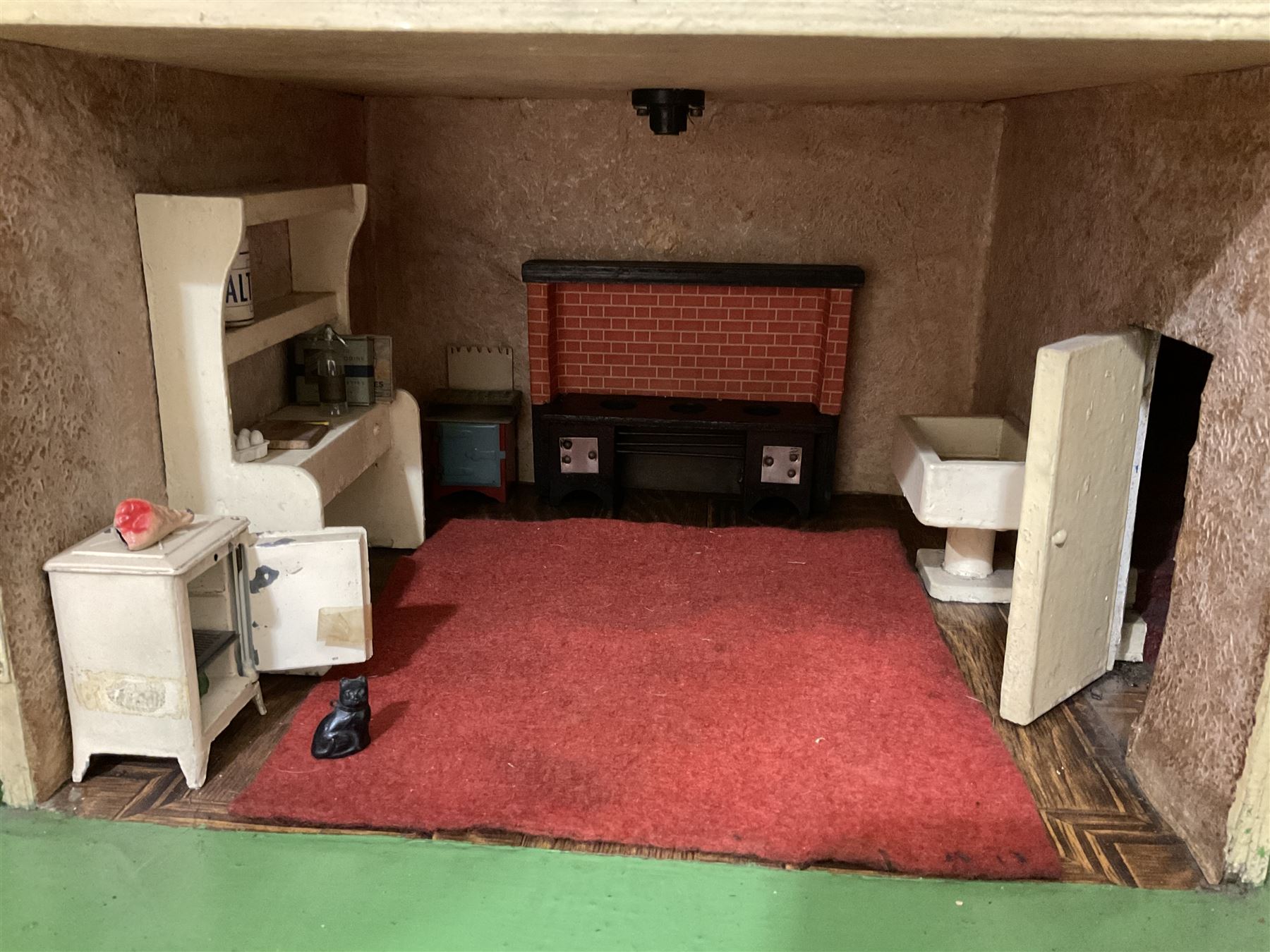 Large Tri-ang No.93 doll`s house in the 'Stockbroker's Range' c1935; two-storey double-fronted Tudor design, half timbered gables, two-storey bay windows, cream and mock shrubbery to front, opening metal framed windows with green shutters, red simulated tiled roof with chimney, integral garage with opening doors, front elevation has four hinged doors opening to reveal two bedrooms with fire places, living room, bathroom and kitchen with built in dresser and sink, entrance hall and staircase, side entrance with porch and seat and sun dial over on chimney stack; some wiring for electrical lighting; metal Tri-ang Toys disc verso; comprehensively furnished H66cm L117cm D43cm